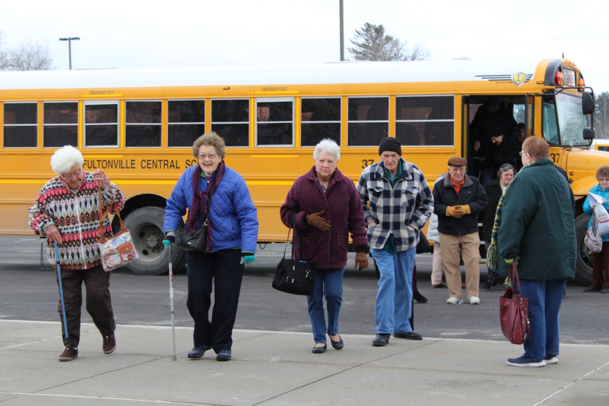 Members of local senior citizens groups exit a school bus onto the district campus.