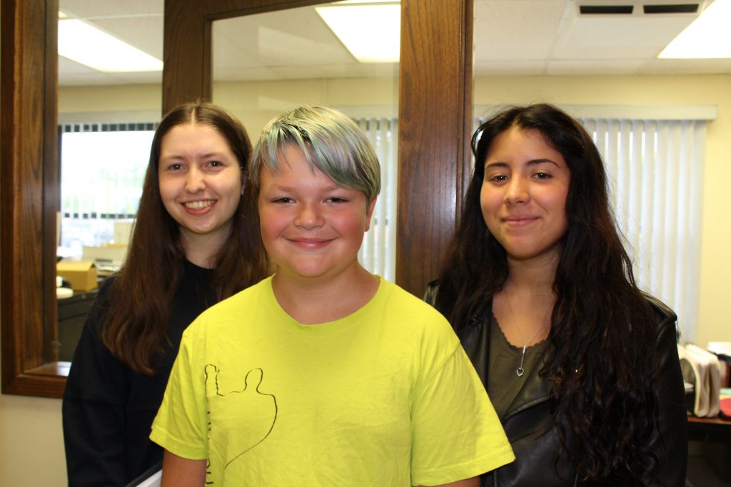 A middle school student is flanked by two high school-aged exchange students