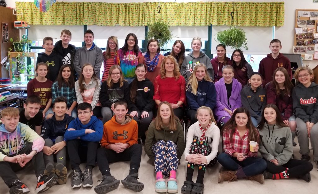 three rows of students pose for a group photo in their teacher's classroom