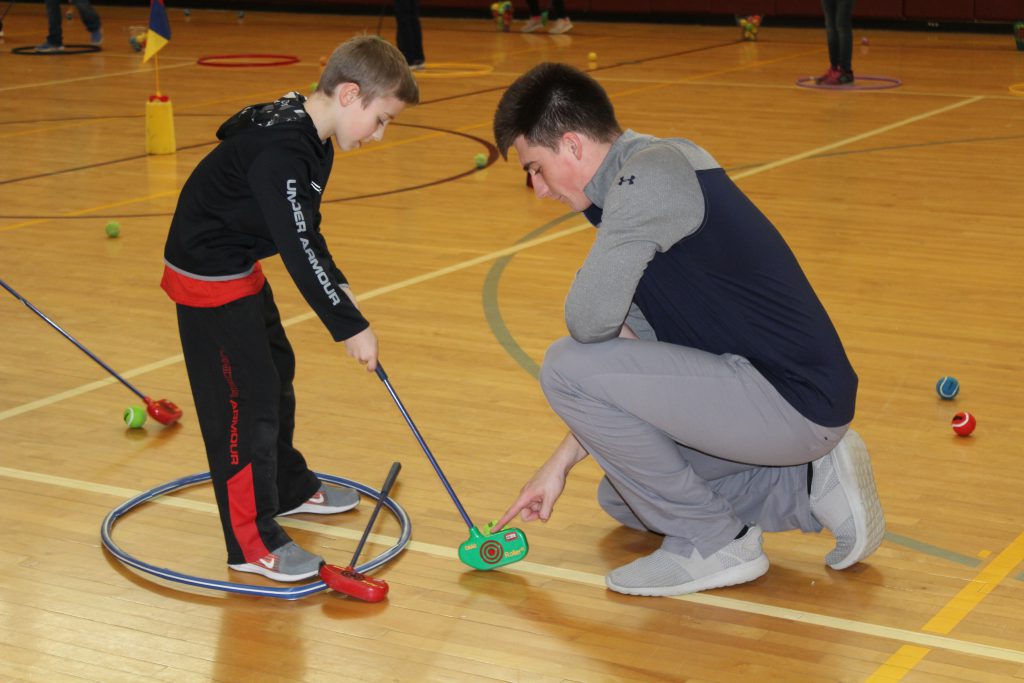 Elementary student learning to golf in gym class with local golfer