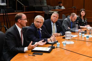 school superintendent speaks in a microphone at a table in a hearing room at the NYS legislature.