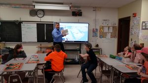 machinist points to a digital map in front of a sixth grade classroom