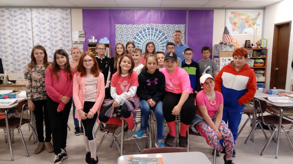 sixth grade students pose on desks for a class photo with a machinist