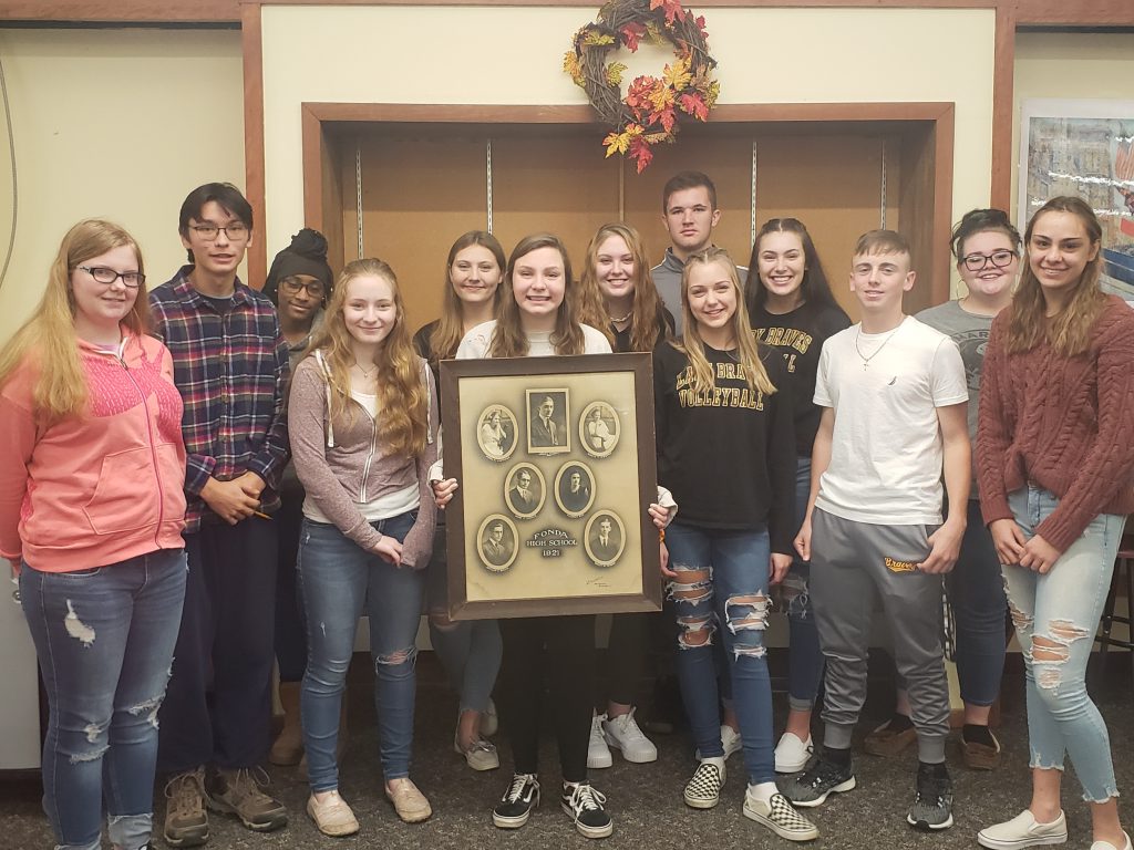 group of high school students pose in a library while holding a picture of the class of 1921