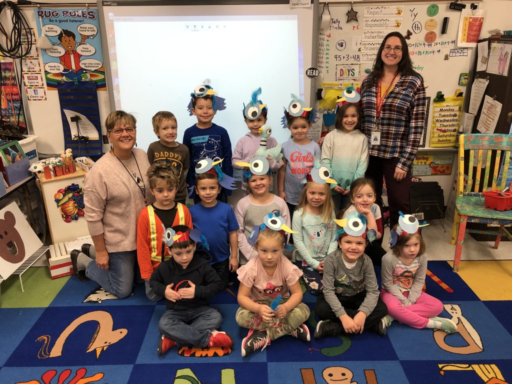 kindergarten class wearing pigeon headbands on a carpet in an elementary classroom