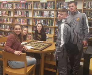 a group of five high school students observe historic photographs at a table in a school library