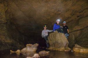 two high school students and their club adviser stand on rock formations in a cave