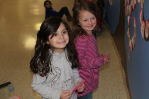 kindergarten students tape hand drawn portraits to a large tree painted on a wall