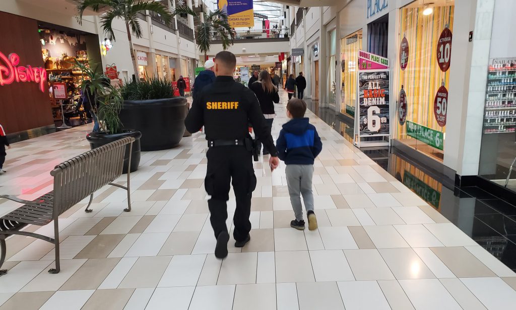 back view of a sheriff's deputy walking through a mall with a third grader