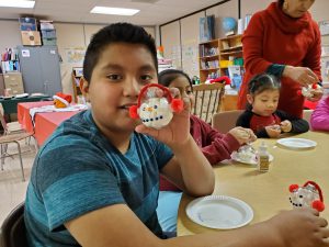 elementary student holds a christmas ornament while sitting at a table in a classroom