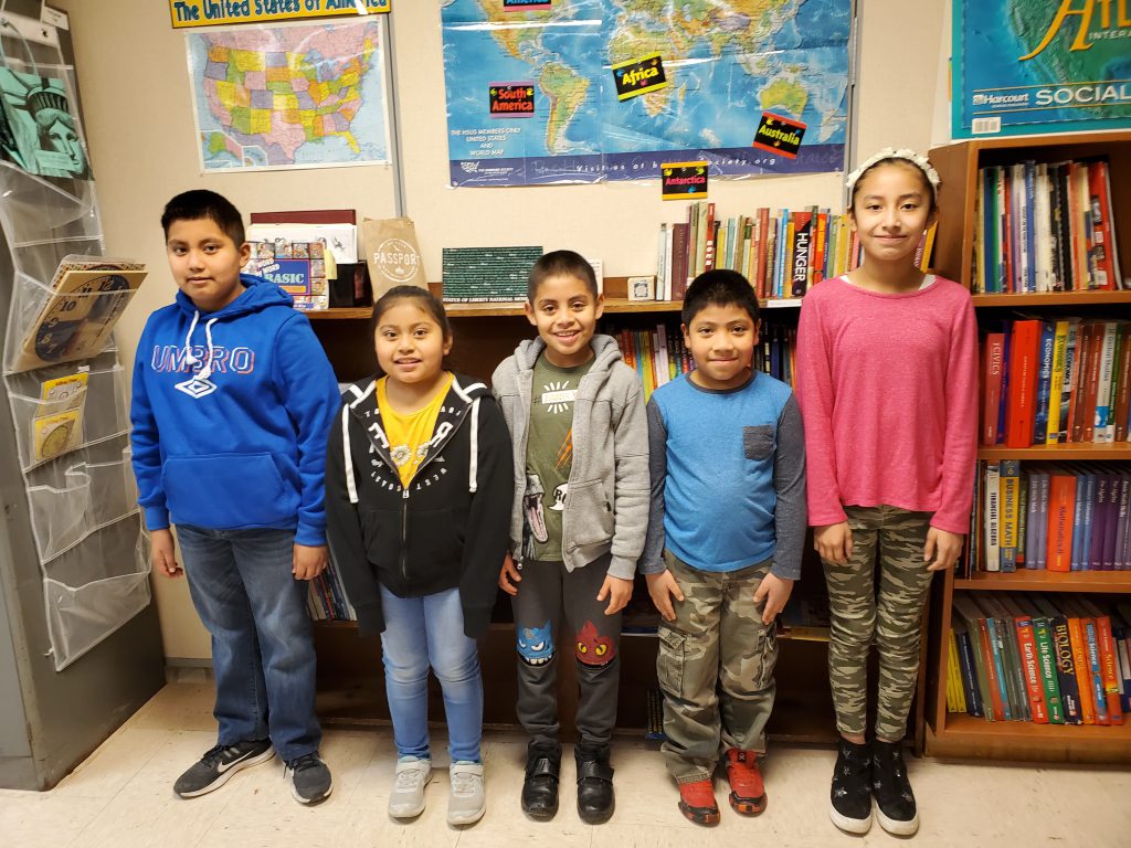 five students stand at the front of a classroom