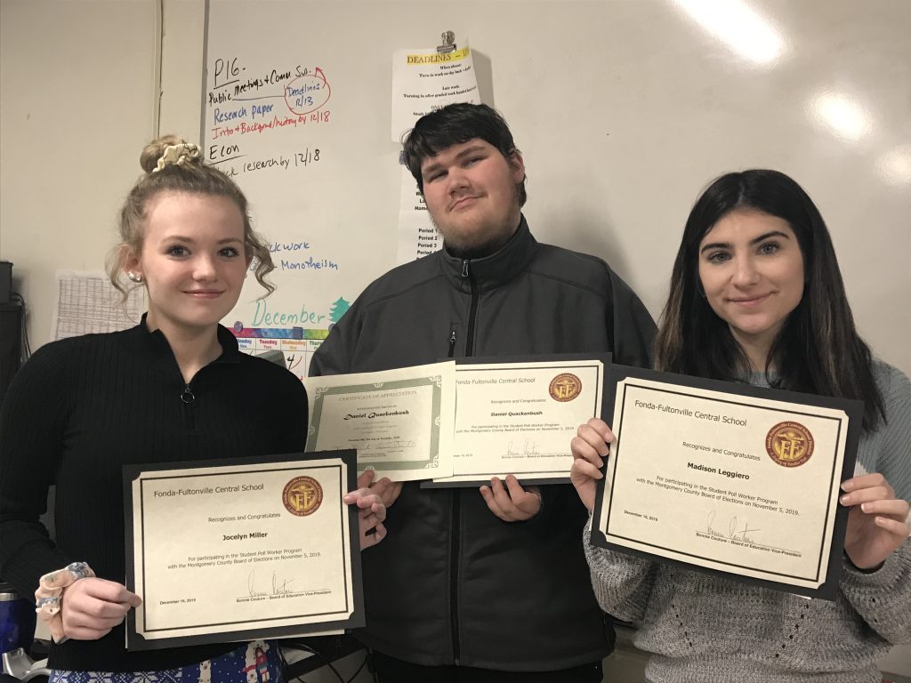 three high school students hold certificates in front of a classroom white board