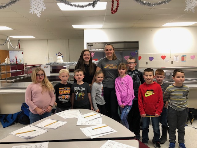 two high school students stand with a group of children in a school classroom