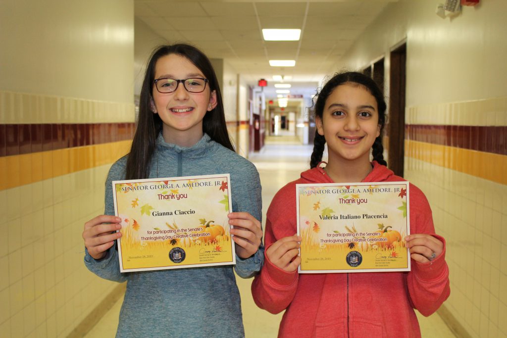 Two middle school students hold certificates in a school hallway