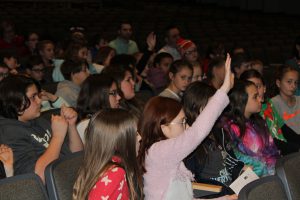 middle school student raises their hand from the audience in a school auditorium