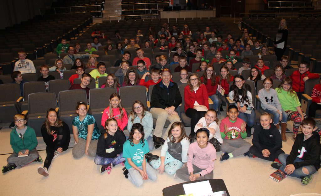 the fifth grade class seated in the audience of a school auditorium with a children's author in the front row
