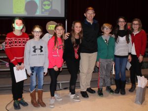 children's author stands in the front of a school auditorium to pose for a photo with seven middle school students
