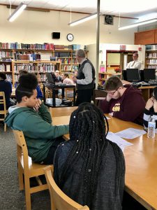 a county election board employees lead a presentation in a school library. students are seated at tables