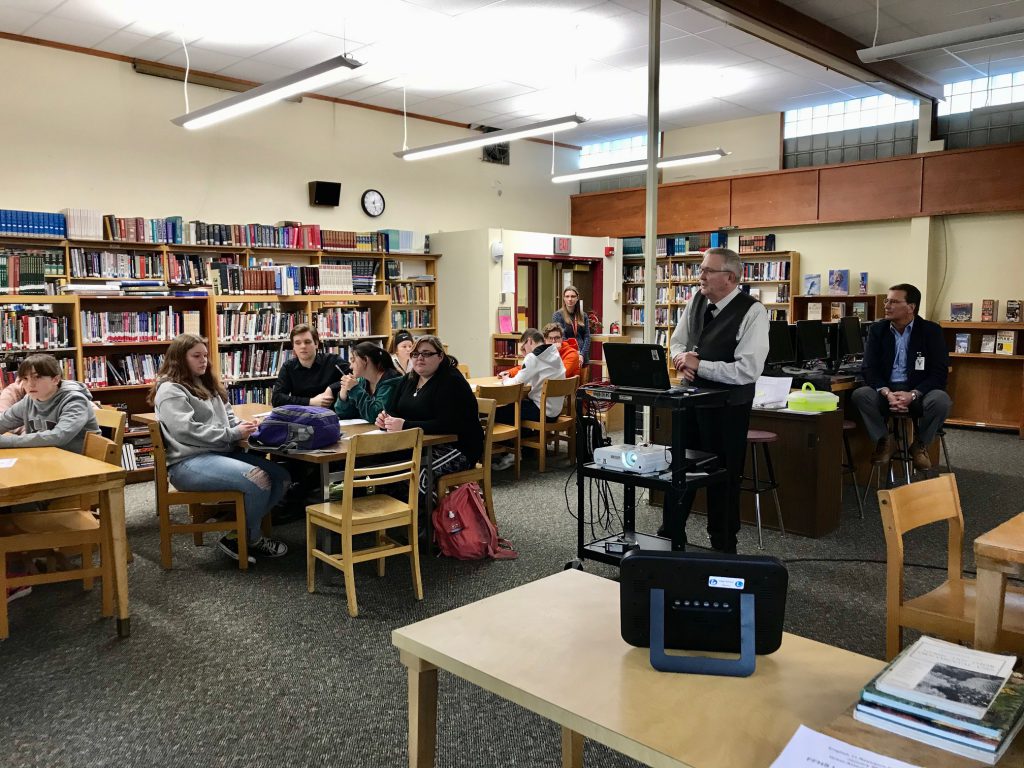 two county election board employees lead a presentation in a school library. students are seated at tables