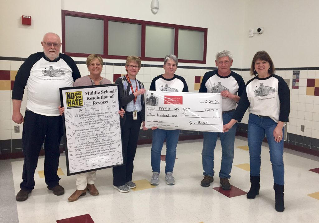 a teacher with members of the community foundation holding a large check display in a school cafeteria