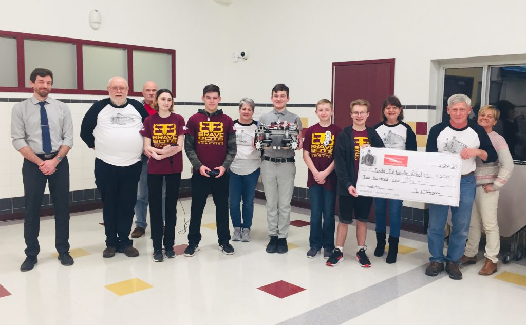 members of a school robotics team with members of the community foundation holding a large check display in a school cafeteria