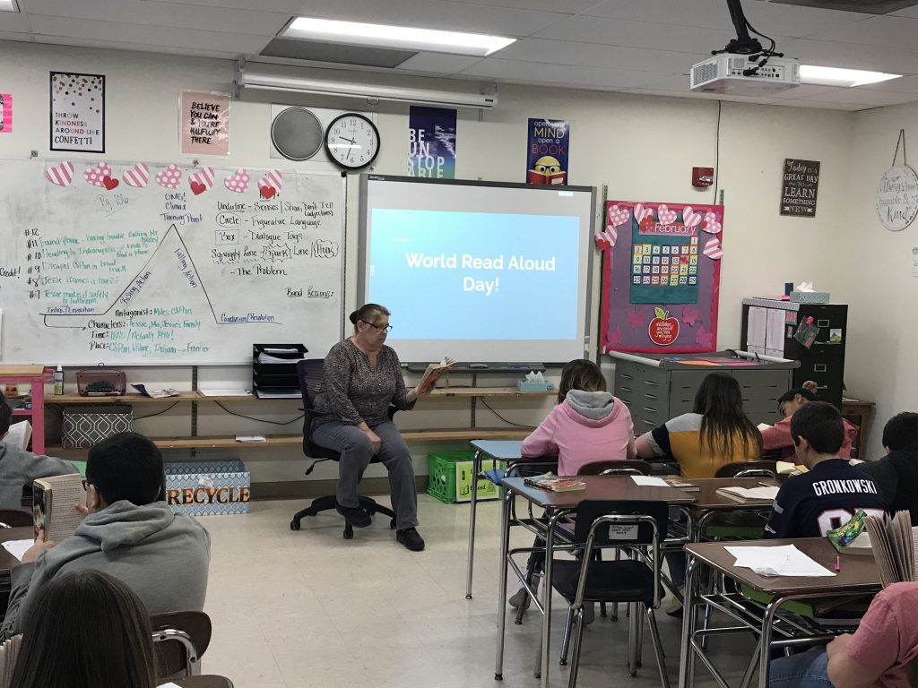 school employee reads to students in the front of a middle school classroom