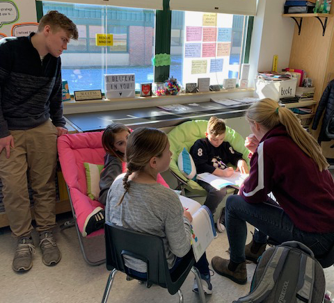 two high school students work with three elementary students in a classroom