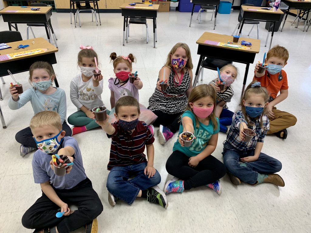 first graders seated on classroom floor wearing face masks and holding up dessert cups