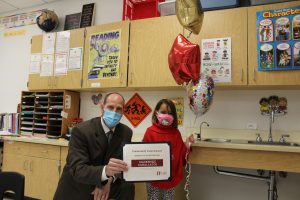 school superintendent and elementary student hold up a certificate and balloons