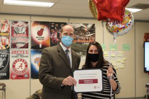 school superintendent and teacher hold up a certificate and balloons