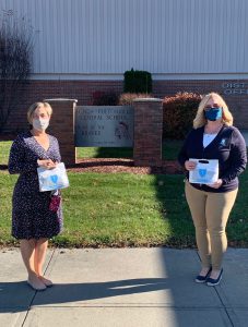 school employee holds a ppe kit while standing outside of the school building with a blueshield employee