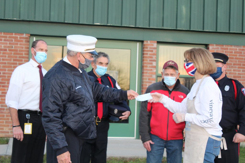 a firefighter in formal dress gives a check to a school teacher outside of a school building