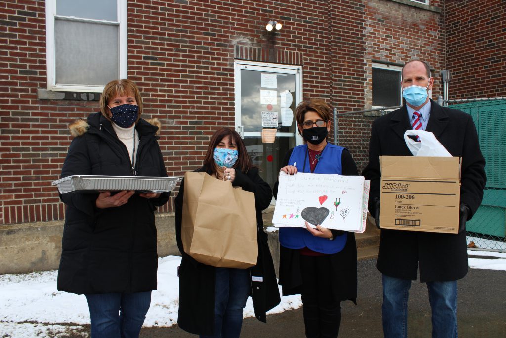 four adults wearing face masks hold bags and boxes of food