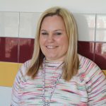 portrait of a mental health counselor with shoulder length blonde hair in a school hallway