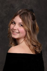 portrait of a high school student wearing a black top looking over their shoulder with shoulder length blonde hair