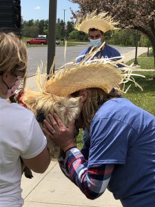 school principal wearing a straw hat leans down to kiss a pig held by a handler