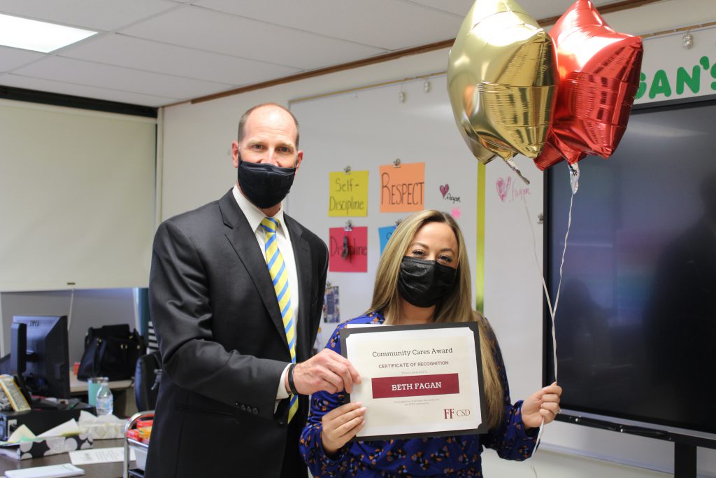 school superintendent stands with a high school teacher holding a certificate and balloons