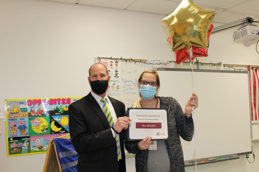 school superintendent stands with an elementary school speech and language pathologist holding a certificate and balloons