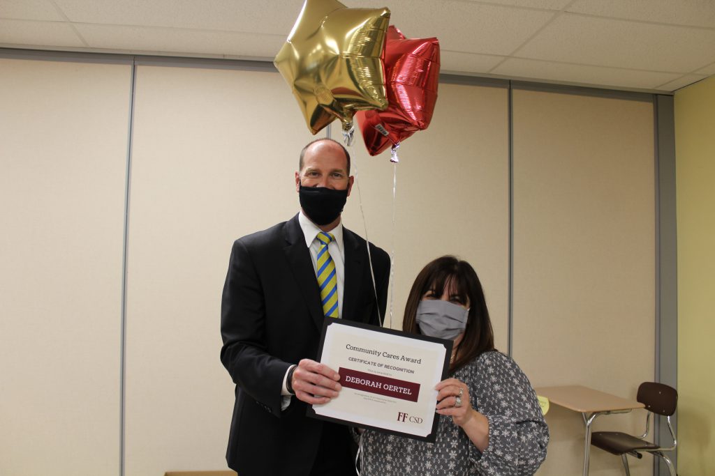 school superintendent stands with a middle school teacher holding a certificate and balloons