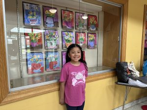 F-F third grade student Maylin Perez Jimenez proudly stands in front of her selected artwork.